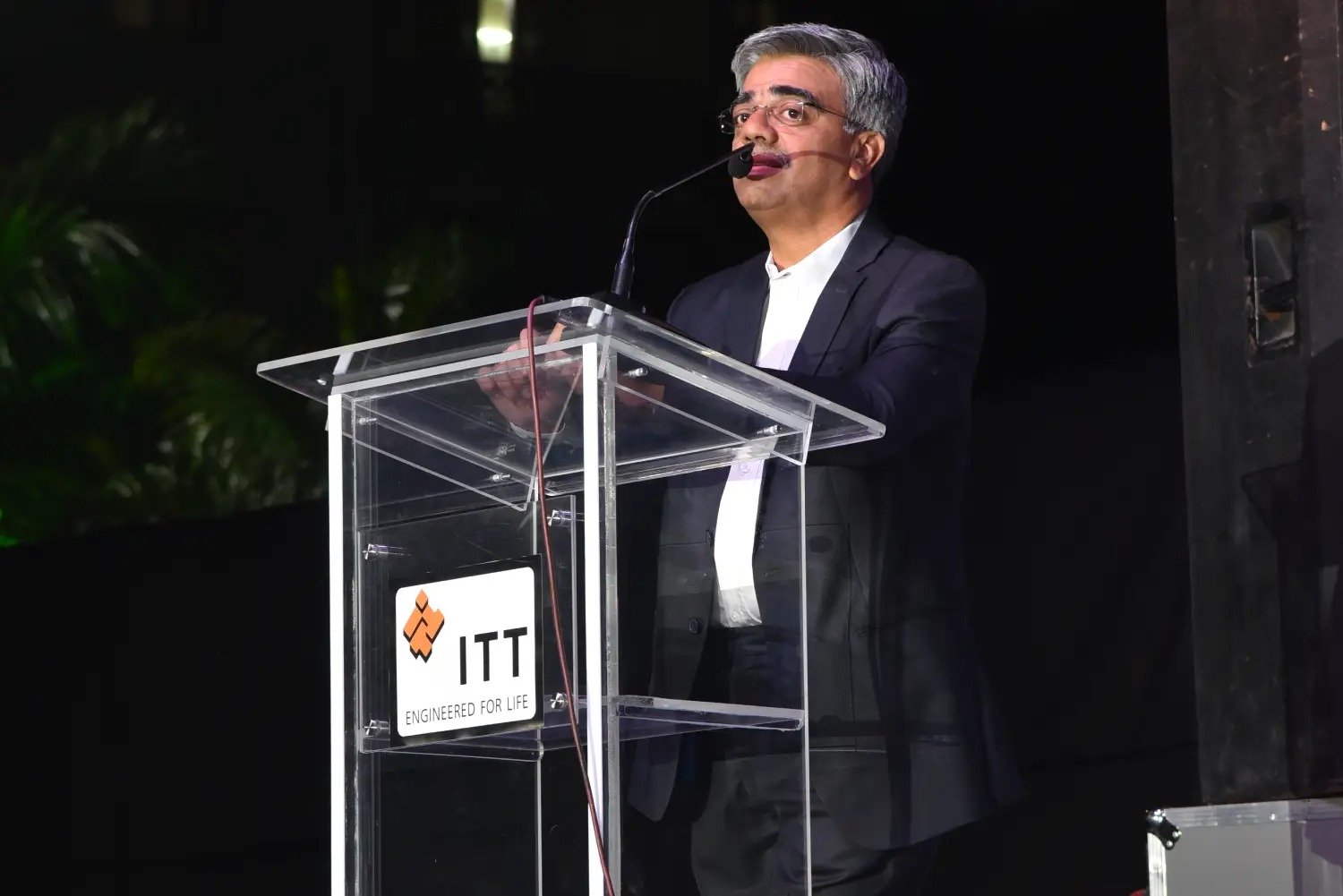 Man in suit speaking at podium with ITT logo on podium